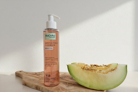 Bottle of Mageau Magnesium Gentle Face Cleanser next to a halved cantaloupe on a wooden surface.